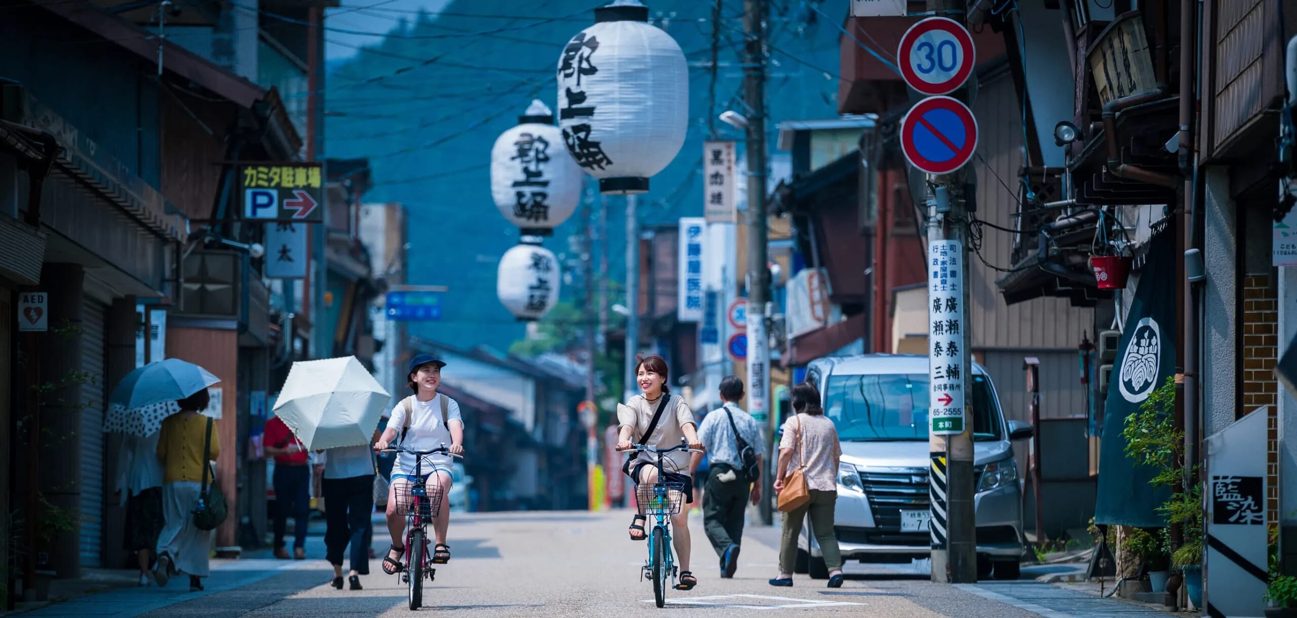 提灯が飾られた通りを自転車で走る2人の女性