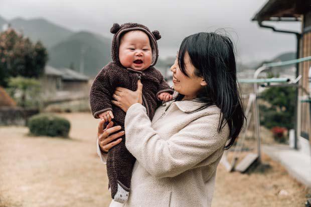 フード付きのカバーオールを着た赤ちゃんを抱っこする母親