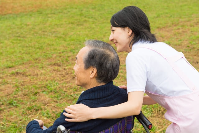 介護職員が車椅子に乗った男性の肩に両手を添えて話しかけている様子