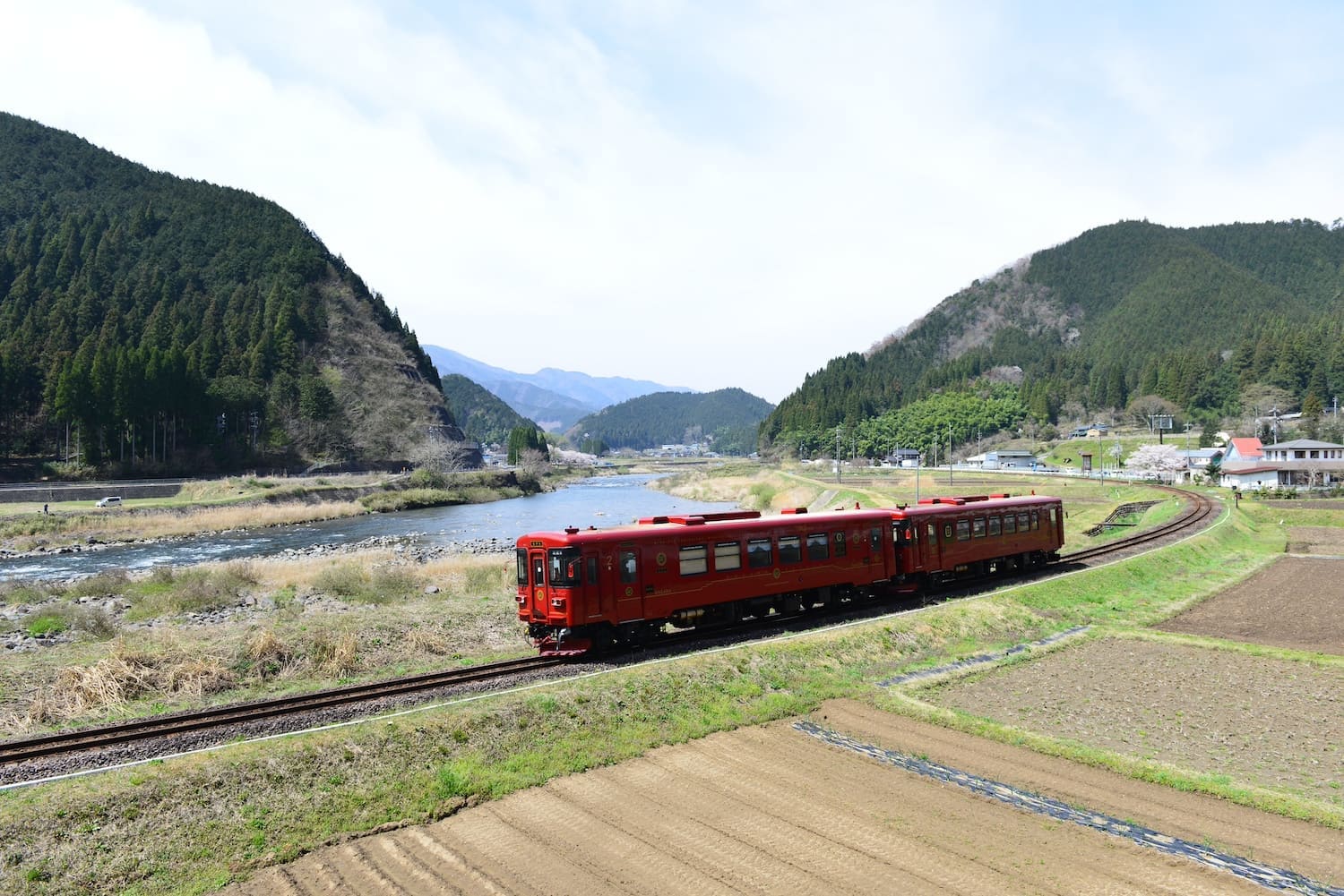 河川敷の土手を走る2両編成の赤い電車